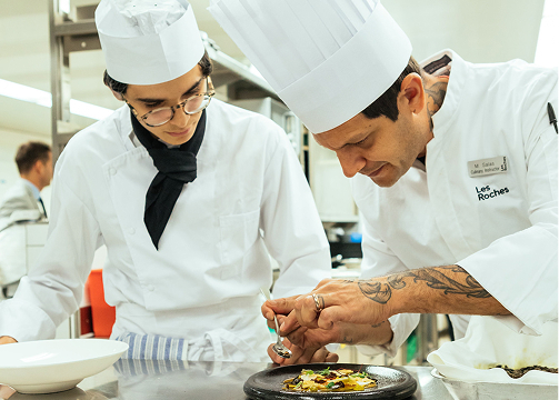a les roches culinary student watches an instructor plate a gourmet dish a les roches culinary student watches an instructor plate a gourmet dish